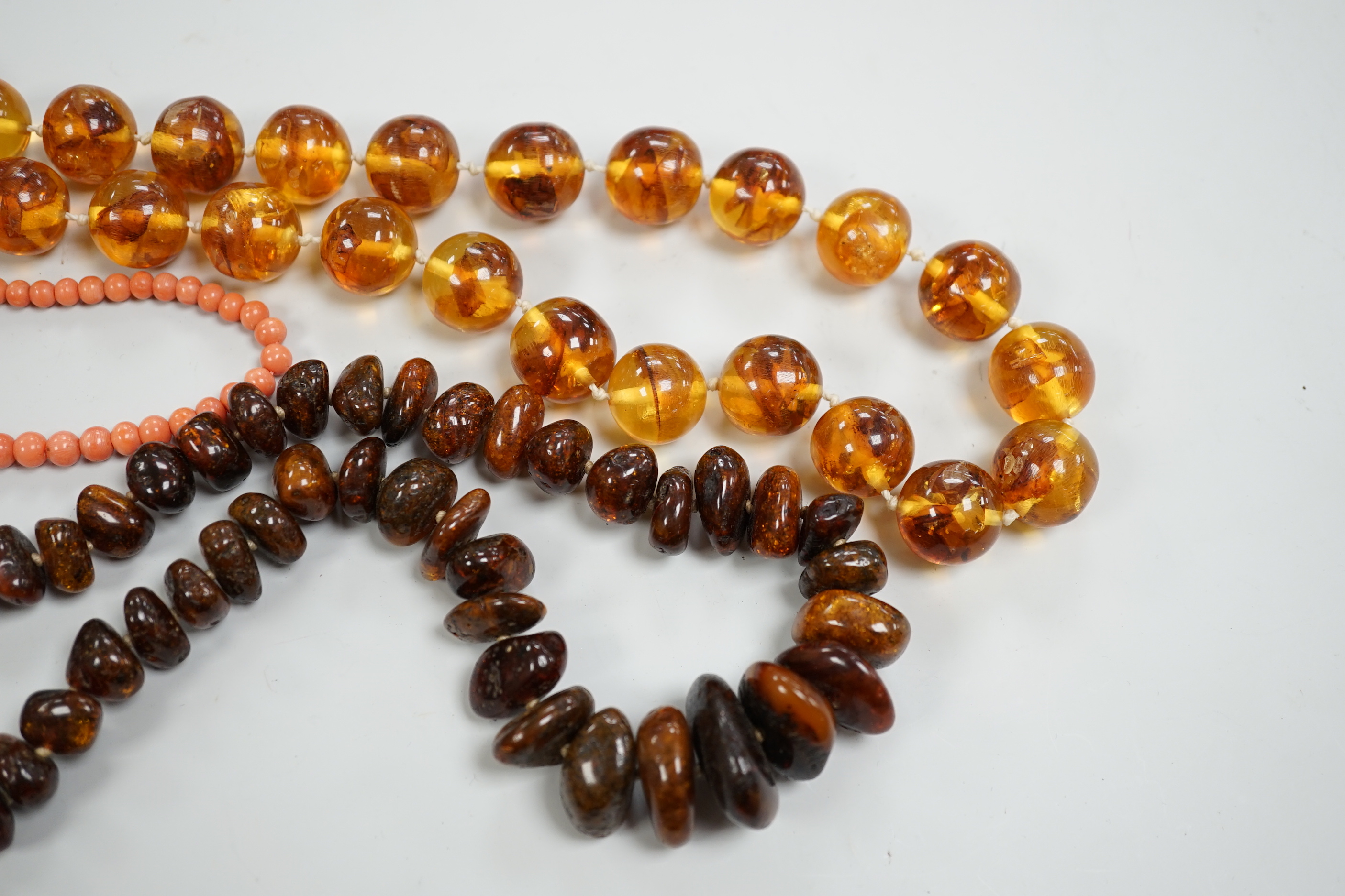 A coral bead necklace, 44cm and two amber bead necklaces.